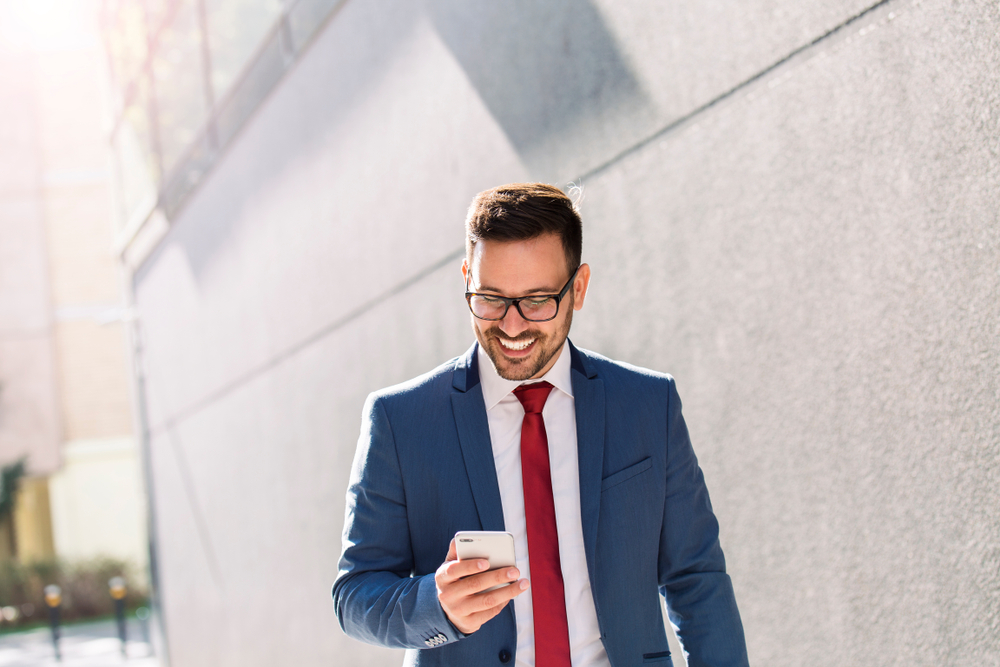 Handsome smiling young businessman reading text message on his phone