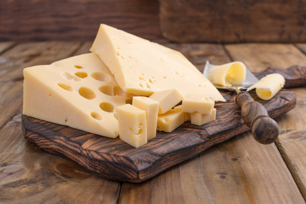 Cheese with holes large and small. Wooden board and knife. Traditional Dutch cheese. Copy space