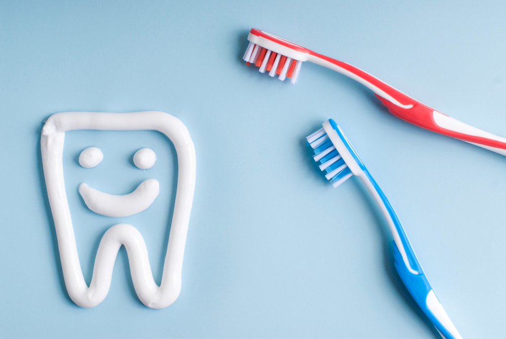 Toothpaste in a form of a smiling tooth. Red and blue toothbrushes. Toothpaste on blue. Dental hygiene.
