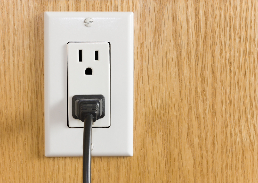 Electrical outlet with black power cord. Home interior electrical outlet with black power cord and plug against wood textured paneling.
