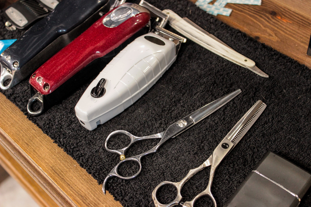 Hairdressing tools. Scissors, thinning scissors, comb, clippers, edging machine. They lie on a wooden table top, on a towel. Barber, mens salon. Barbershop. 