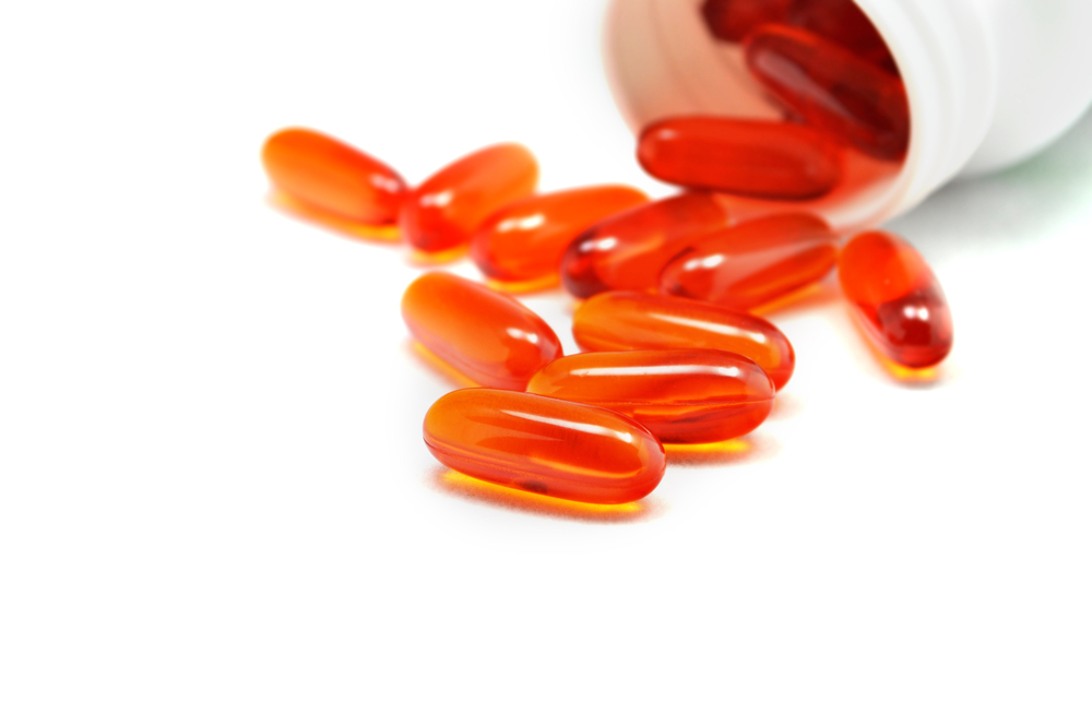 Wild Alaskan Salmon Oil soft gel capsules spilling out of a jar. These fish oil pills are high in Vitamin D, Vitamin A, and Omega 3