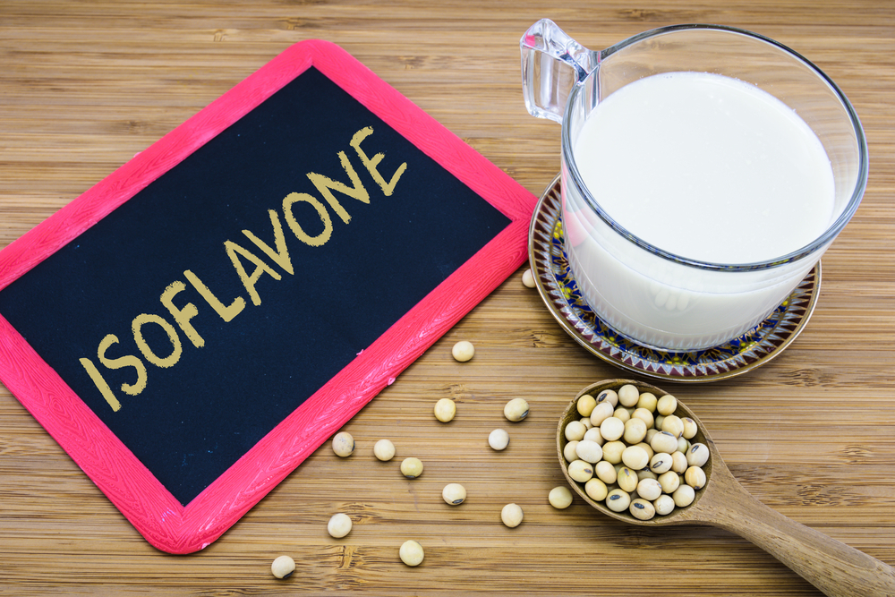 Isoflavone written on chalkboard with a cup of soy milk and soybeans on wood background