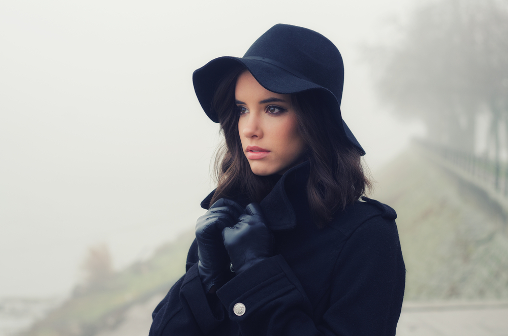 Beautiful sad girl in black clothes, black hat and leather gloves outdoor on moody winter day.