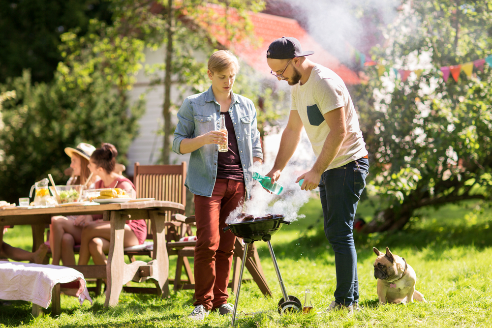 leisure, food, people and holidays concept - friends cooking meat on barbecue grill at summer outdoor party