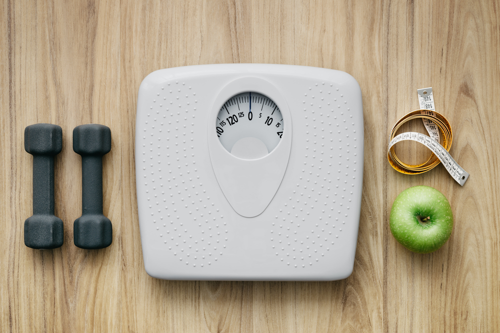Weight scale, healthy snack, measuring tape and dumbbells on a table, weight loss and sports concept, flat lay