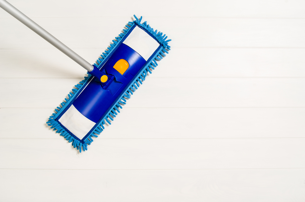 Cleaning floor with mop top view. Microfiber mop isolated on white wooden floor background. Home cleaning product concept photograph with copy space
