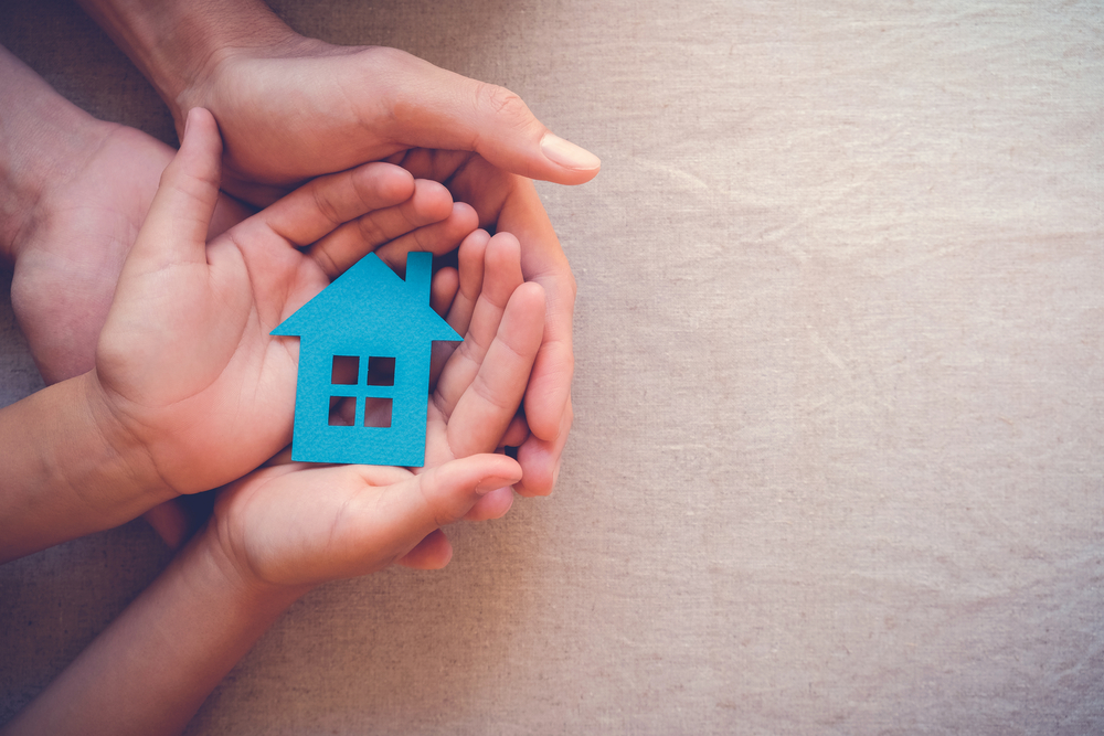 Adult and child hands holding paper house, family home, homeless housing and real estate, insurance concept