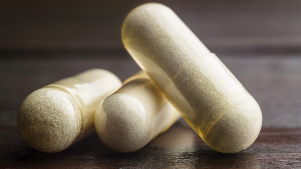 White capsules of glucosamine chondroitin, healthy supplement pills on wooden table, macro image.